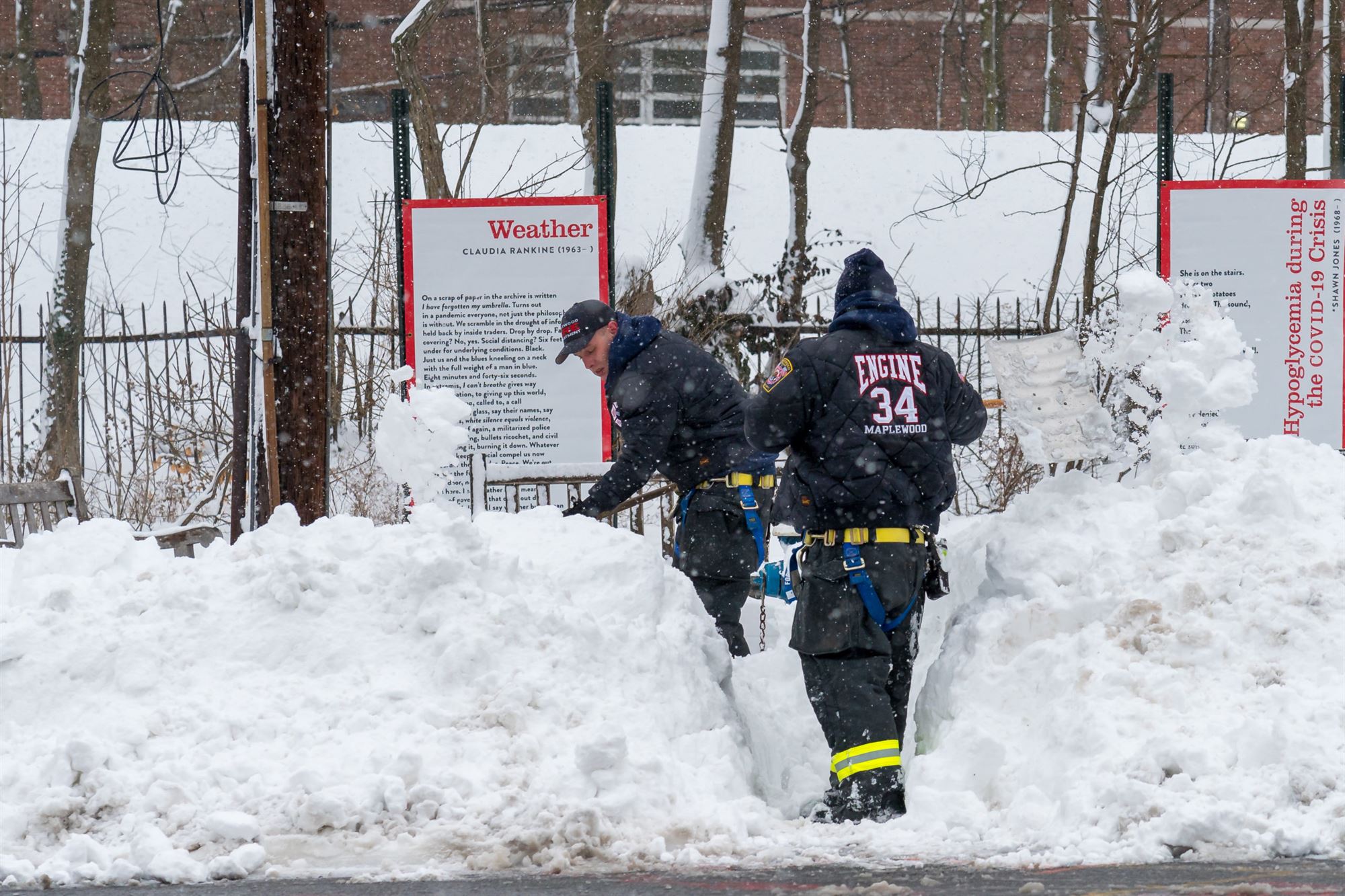 Firefighters shovel snow near sign with a poem